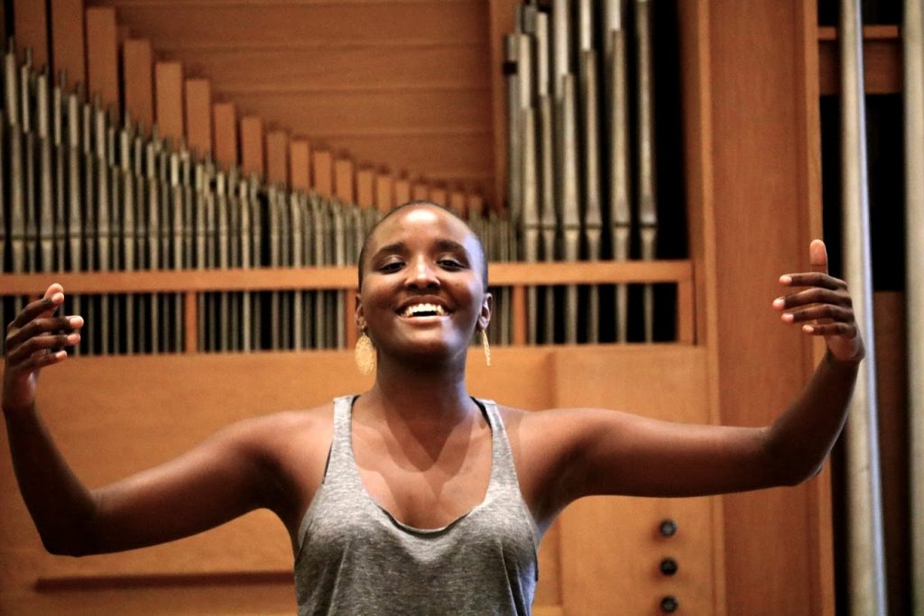 Faith Jones sings, smiling with her arms out wide, the organ of Person Hall in the background.