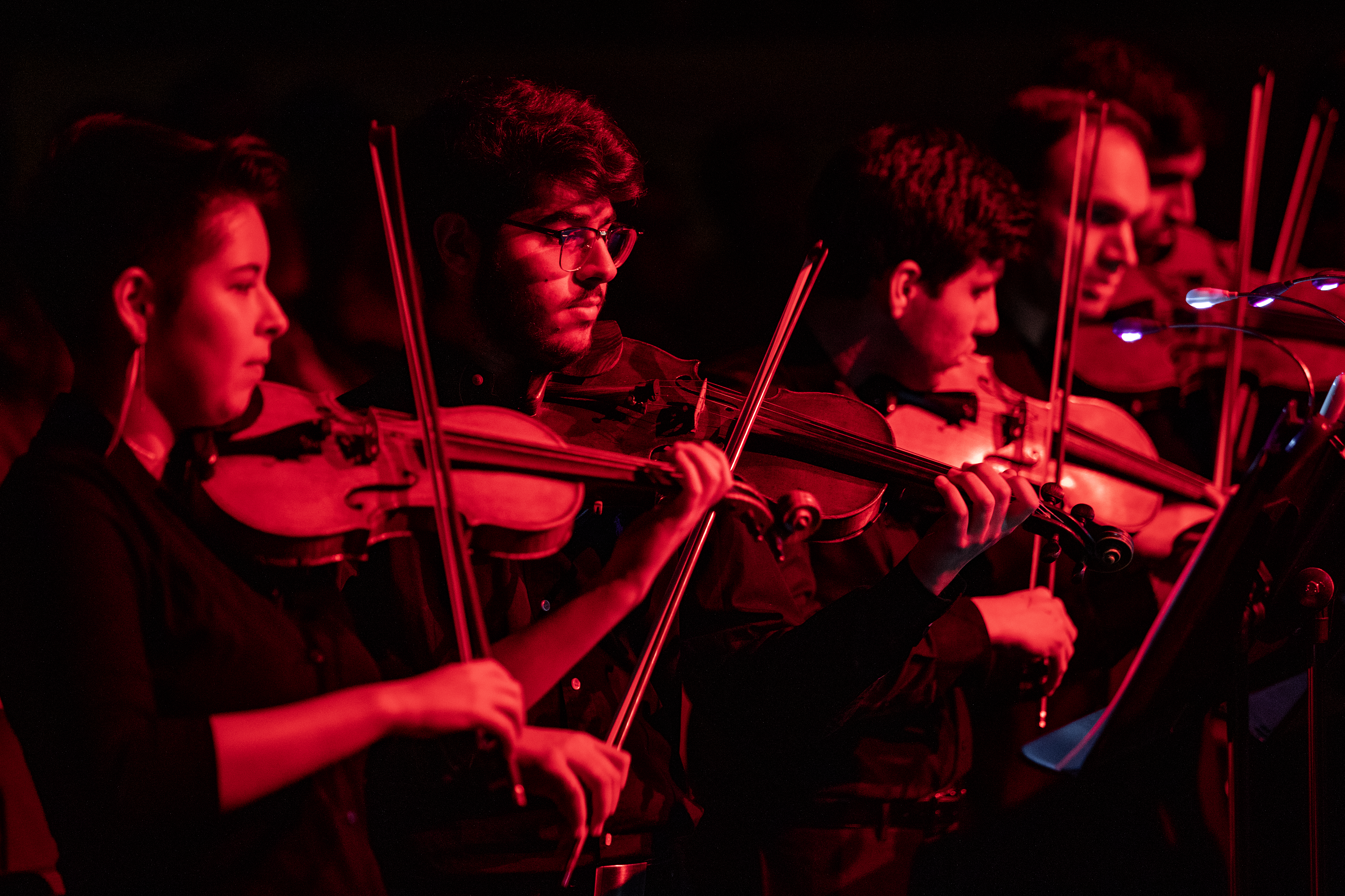 Violinists perform, bathed in red light.