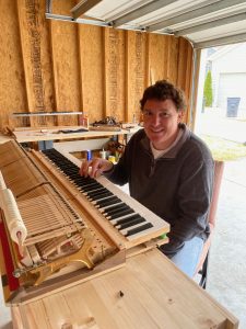 Max poses with a piano deconstructed for maintenance in his home workshop.