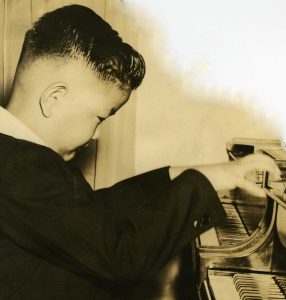 A young Francis plays the piano, his hands hovering in mid-air over the keys as he looks at them intently.