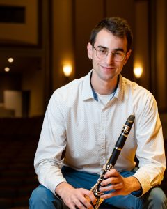 Matthew Svec sits smiling and holding his clarinet in Moeser Auditorium.