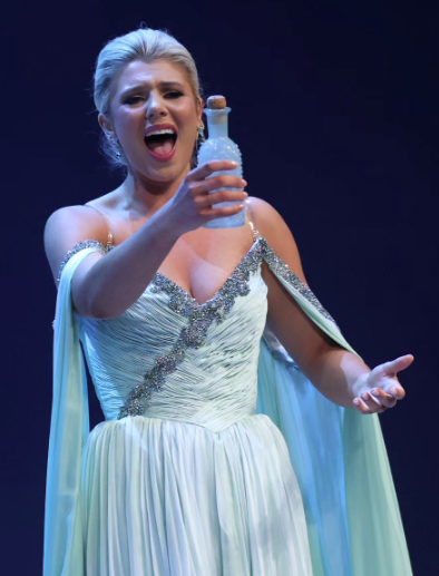 Taylor Loyd holds a bottle out as she sings her aria during the talent portion, wearing a white gown with silver beading on the trim.